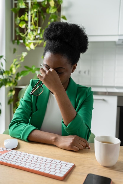 Wyczerpana czarna kobieta freelancer wycierająca oczy po długich godzinach pracy przy komputerze ma problem ze wzrokiem