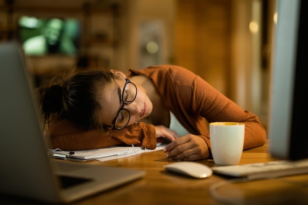 Wyczerpana kobieta drzemiąca na biurku podczas pracy do późnych godzin nocnych w domu