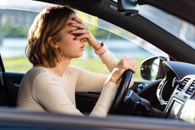Zdjęcie wyczerpana kobieta kierowca czuje ból głowy siedząc w samochodzie trzymając rękę do głowy i czując niepokój
