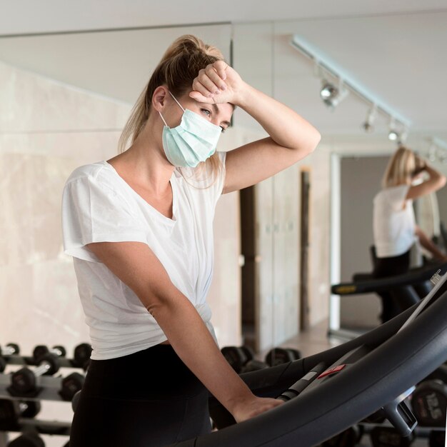 Wyczerpana kobieta z maską medyczną na siłowni