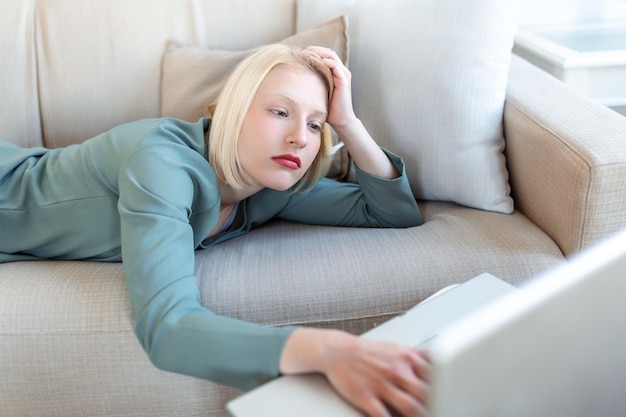 Wyczerpana młoda kobieta leżąca na kanapie przy laptopie zbyt zmęczona lub znudzona pracą online w domu wolna przestrzeń Pracoholizm chroniczne zmęczenie przepracowanie koncepcji pracy zdalnej