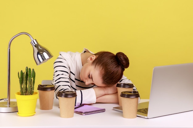Wyczerpana, zmęczona kobieta, kierownik biura, śpiąca w miejscu pracy, leżąca w otoczeniu filiżanek z kawą