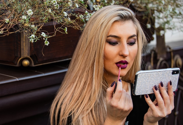 Zdjęcie wygląda modnie. kosmetyki i makijaż. podążaj za moją modą. przygotować się na randkę lub spotkać. zawsze dobrze wyglądać. blond piękności używać telefonu jako lustra. blog o modzie samouczka makijażu. seksowna pani położyła szminkę na ustach.