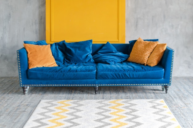 Wygodna klasyczna niebieska kanapa z pomarańczowymi poduszkami w prostym minimalistycznym mieszkaniu
