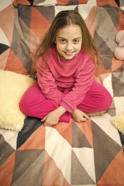 Wygodna piżama na relaks Dziewczynka małe dziecko nosi miękką śliczną piżamę podczas relaksu na łóżku Uśmiechnięte dziecko relaksuje Piżamy i ubrania do domu Piżamy i tekstylia do sypialni Dziecko ciesz się wypoczynkiem