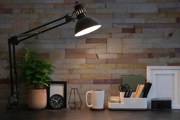 Wygodne miejsce pracy z papierową lampką na filiżankę kawy i ramką na zdjęcie na czarnym stole z ceglaną ścianą