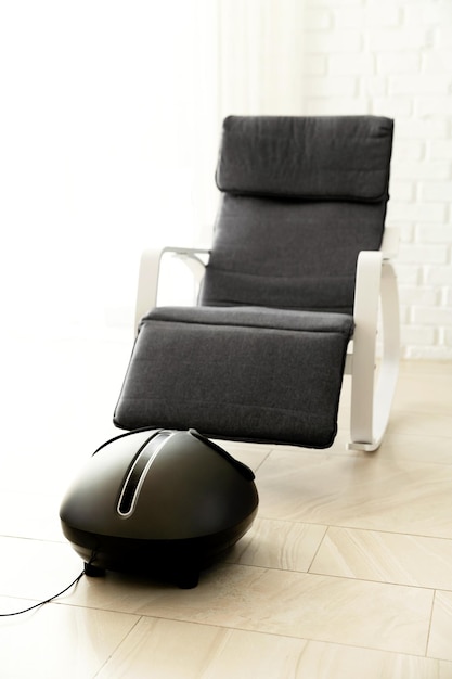Wygodny elektryczny masażer do stóp stoi w pobliżu bujanego fotela w domu koncepcja masażu relaksacyjny masaż stóp