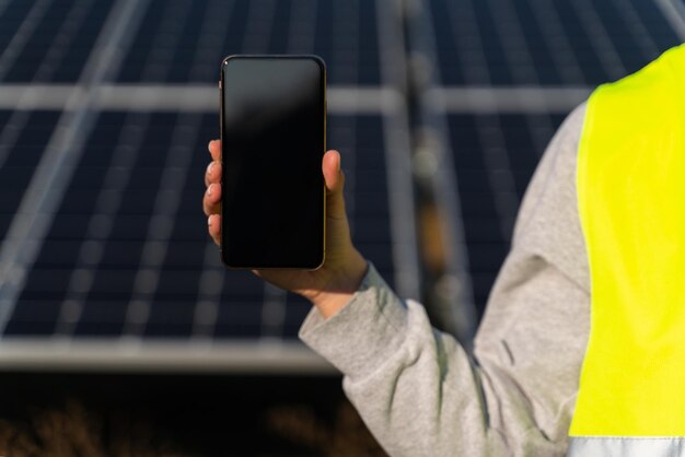 Wykadrowany widok kobiety inżynier inspektor w mundurze trzymającej smartfon na elektrowni słonecznej Solarfarm