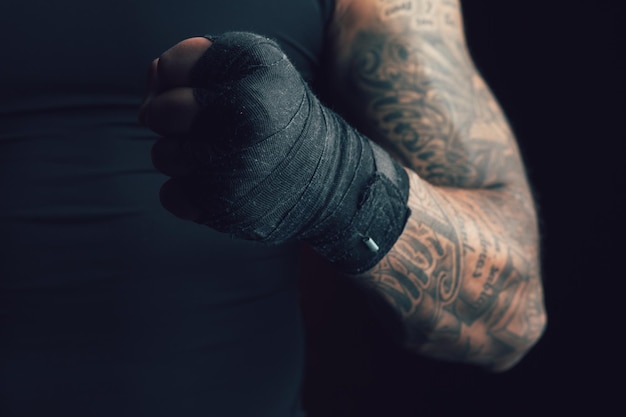 Wykadrowany wizerunek wytatuowanego sportowca z silnymi mięśniami zaciskającymi pięść z bandażem