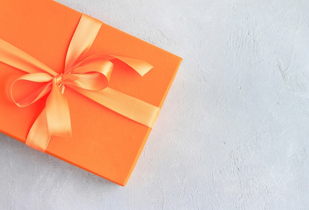 Wykonaj papierowy prezent z pomarańczową wstążką na szarym tle z miejsca kopiowania.