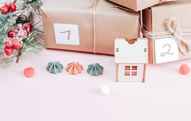 Wykonaj prezenty z numerami 1 2 przewiązane nitką jutową gałązka świerkowa drewniany dom i ciasteczka na różowym tle