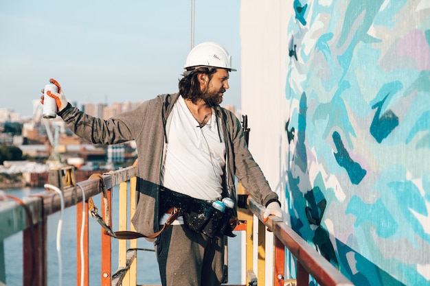 Wykonawca, artysta na dużej wysokości w kołysce budynku wykonuje malowanie elewacji