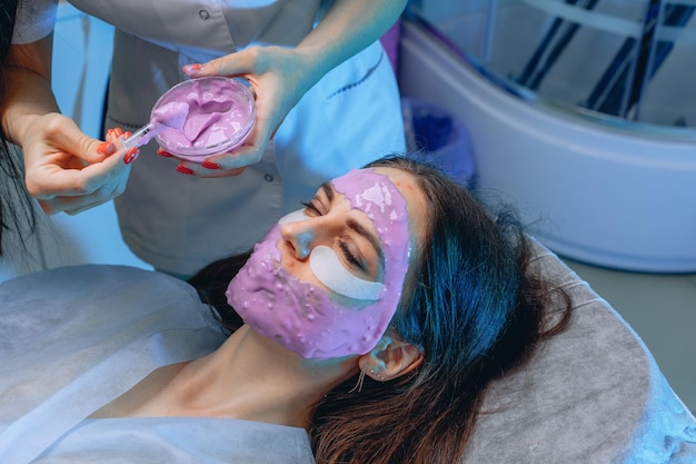 Wykwalifikowana kosmetolog wykonuje dla klienta maskę alginianową na całej twarzy, aby skóra była gładsza i zdrowsza.