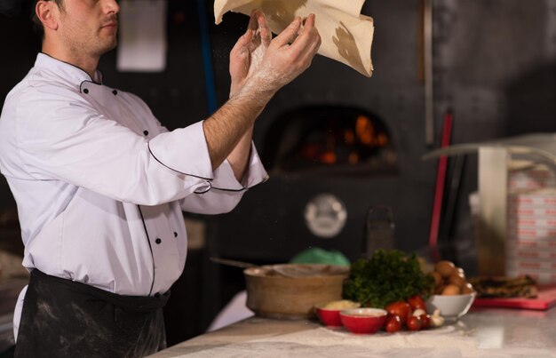 Wykwalifikowany kucharz przygotowujący ciasto do pizzy wałkuje rękami i wymiotuje