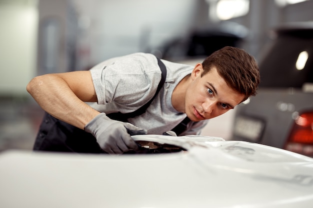 Wykwalifikowany młody mechanik naprawia biały samochód w serwisie samochodowym.