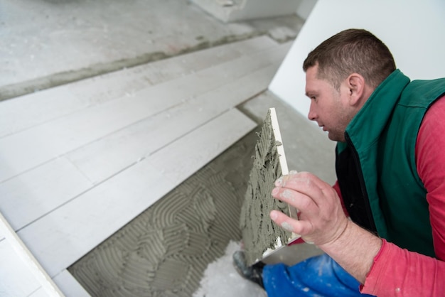 Wykwalifikowany pracownik instalujący płytki ceramiczne z efektem drewna na podłodze Pracownik wykonujący podłogi laminowane na placu budowy nowego mieszkania