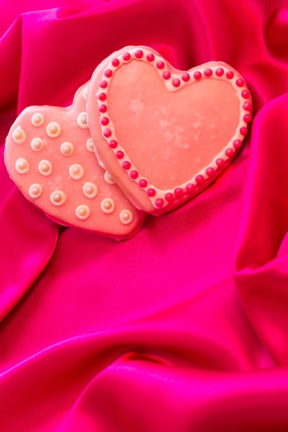 Wykwintne ciasteczka w kształcie serca ozdobione na Walentynki na różowym jedwabiu.