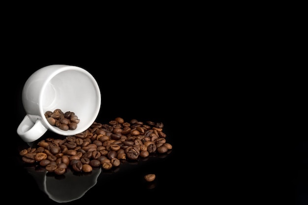 Wylane ziarna kawy z filiżanką na czarnym tle.
