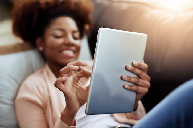 Wyluzowana dzięki swojej ulubionej technologii Ujęcie zrelaksowanej młodej kobiety korzystającej z cyfrowego tabletu na sofie w domu