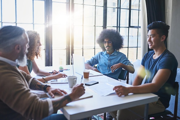 Wymiana pomysłów Ujęcie grupy wesołych, kreatywnych biznesmenów spotykających się razem przy stole w biurze w ciągu dnia