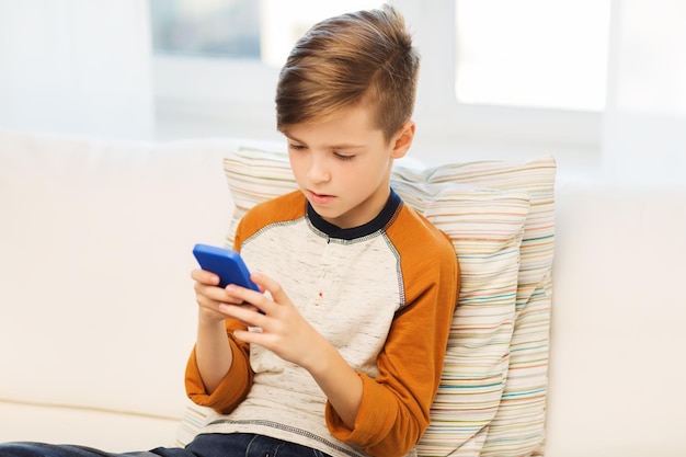 wypoczynek, dzieci, technologia, komunikacja internetowa i koncepcja ludzi - chłopiec ze smartfonem wysyłający wiadomość tekstową lub grający w grę w domu