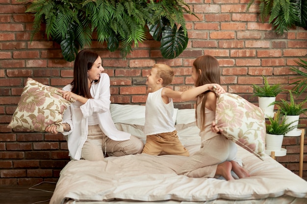 Wypoczynek Rodzinny. Mama Syn I Córka Walczą Na Poduszkach Na łóżku W Sypialni. Radość I Zabawa