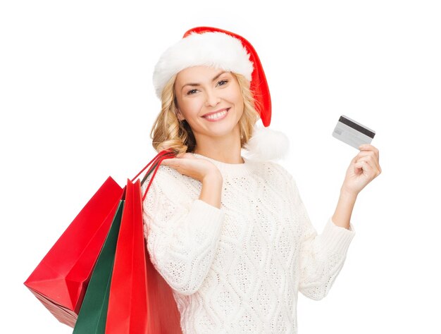 wyprzedaż, prezenty, święta, koncepcja bożonarodzeniowa - uśmiechnięta kobieta w kapeluszu pomocnika mikołaja z torbami na zakupy i kartą kredytową
