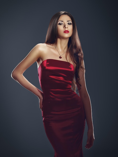 Wyrafinowana elegancja Modna modelka pozuje zmysłowo w dopasowanej czerwonej satynowej sukience na ciemnym tle