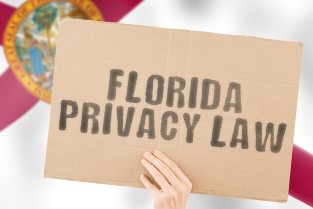 Wyrażenie „Prawo prywatności Florydy” na banerze w męskiej dłoni z flagą Florydy Rynek prywatny