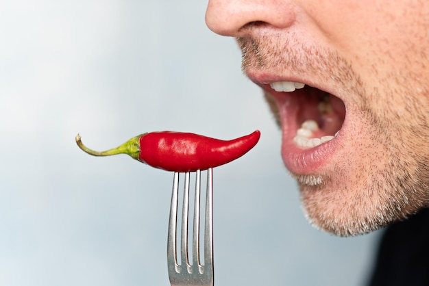 Zdjęcie wyraźny i zabawny człowiek trzymający w ustach czerwoną paprykę paprykową człowiek jedzący pikantną paprykę na niebieskim tle ekstra gorąca papryka cayenne