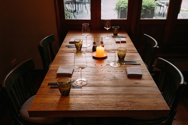 Wyśmienity drewniany stół z sztućcami, kieliszkami do wina, serwetkami, serwetkami i zapaloną świecą na stole.