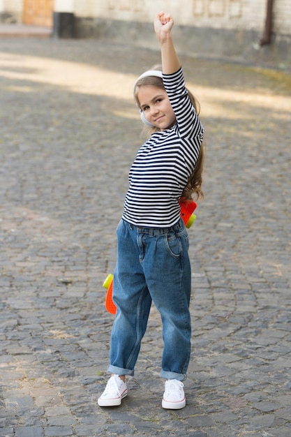 Wysoka wydajność. Dumny skater podniósł rękę z zaciśniętą pięścią. Mała dziewczynka z deską grosza na zewnątrz. Sztuczka Power Slide. Jazda na deskorolce i transport. Zabawna aktywność fizyczna. Silny i zdrowy.