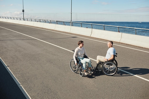 Wysoki kąt portret dorosłej pary na wózkach inwalidzkich, rozmawiającej na świeżym powietrzu i cieszącej się życiem w mieście
