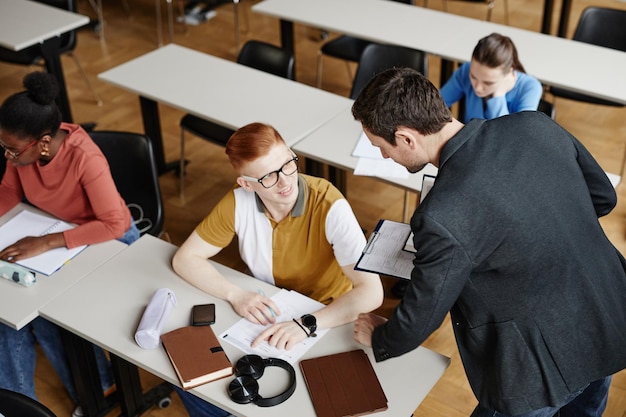 Wysoki kąt portret profesora płci męskiej, pomagający studentom w kopiowaniu przestrzeni w klasie uniwersyteckiej