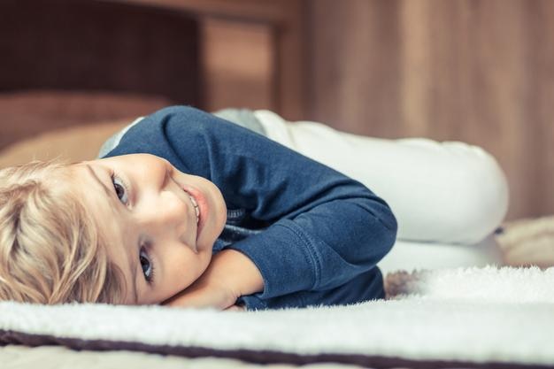 Wysoki kąt portretu uroczego uśmiechniętego chłopca leżącego w łóżku w domu