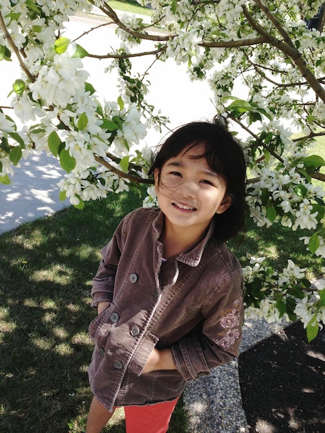Zdjęcie wysoki kąt portretu uśmiechniętej dziewczyny stojącej na drzewie w parku