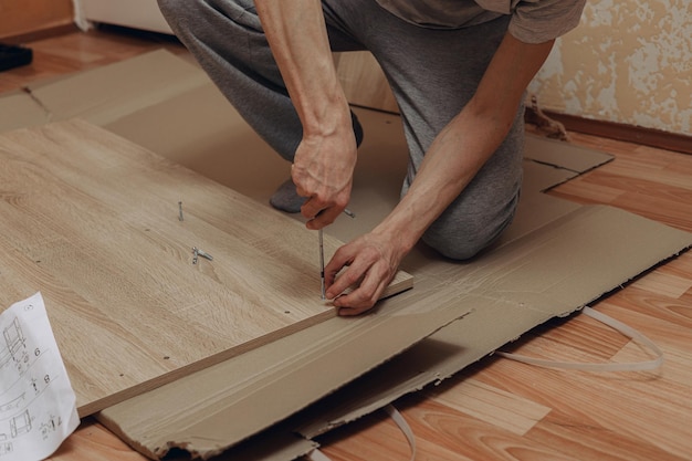 Wysoki kąt przycinania człowieka montującego drewniane meble za pomocą śrubokręta na podłodze w domu