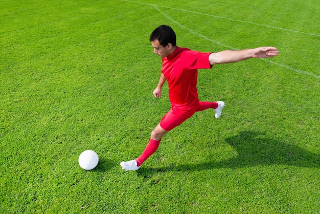 Zdjęcie wysoki kąt widoku człowieka kopającego piłkę nożną na boisku w słoneczny dzień