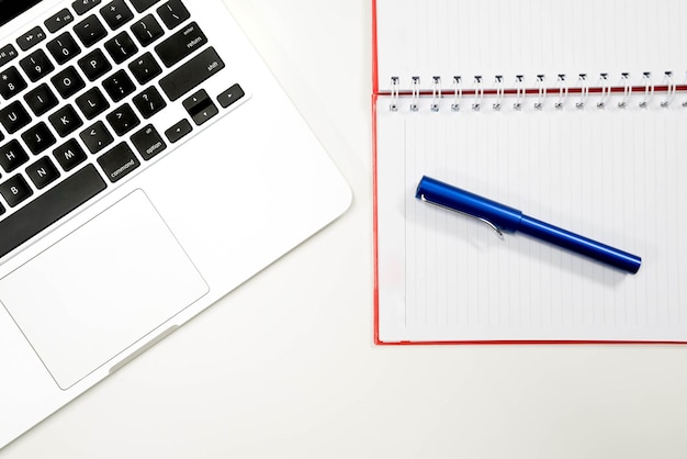 Wysoki kąt widoku laptopa z notatnikiem i długopisem na białym tle
