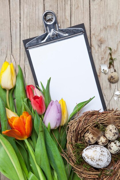 Zdjęcie wysoki kąt widoku schowka z wielokolorowymi tulipanami z jajkami w gnieździe na stole