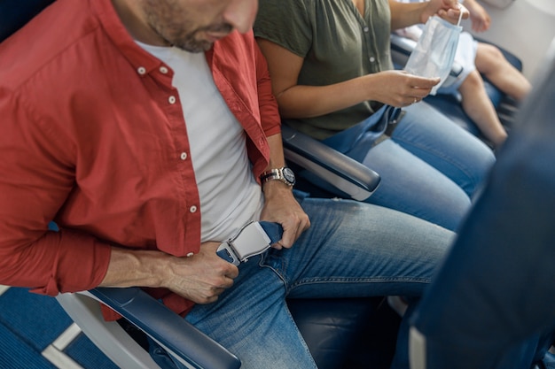 Wysoki kąt widzenia męskiego pasażera zapinającego pas bezpieczeństwa podczas siedzenia w samolocie dla bezpiecznego lotu. Bezpieczeństwo, koncepcja podróży