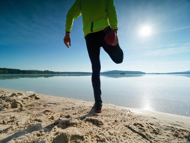 Wysoki, szczupły mężczyzna rozciąga się na plaży w słoneczny poranek. Ciało rozciąga się przed uprawianiem sportu.