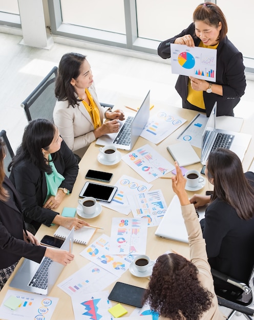 Wysoki widok na sześć kobiet biznesu pracujących i jedną kobietę przedstawiającą wykresy i dokumenty z wykresami z tabletami i laptopami na stole. Koncepcja spotkania biznesowego.