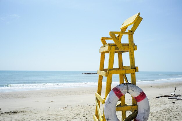 Wysokie drewniane krzesło dla ratownika na plaży z krajobrazem morskim i wybrzeżem w tle