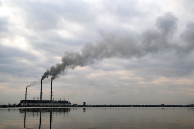 Wysokie Rury Elektrowni Węglowej Z Czarnym Dymem Unoszące Się W Górę, Zanieczyszczające Atmosferę Z Jej Odbiciami W Wodzie Jeziora.