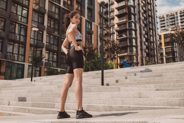 Wysportowana dziewczyna w obcisłej odzieży sportowej stojąca na miejskim tle