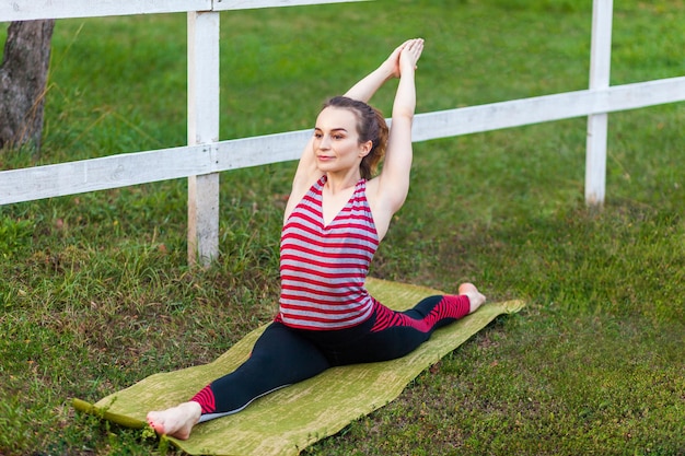 Wysportowana kobieta ćwicząca jogę w parku, wykonująca ćwiczenia boga małp, dzieli pozę hanumanasana