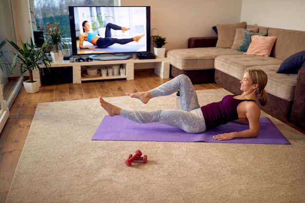 Wysportowana kobieta ćwicząca passe abs podczas treningu przed telewizorem w domu