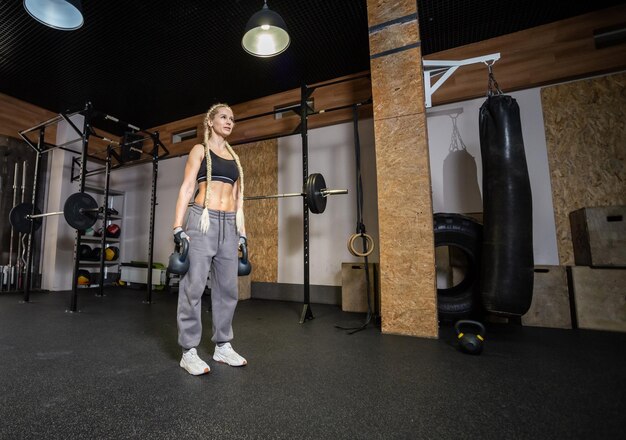 Wysportowana kobieta ćwiczy z ciężkim kettlebell w nowoczesnej siłowni Funkcjonalny trening mięśni Szeroki kąt