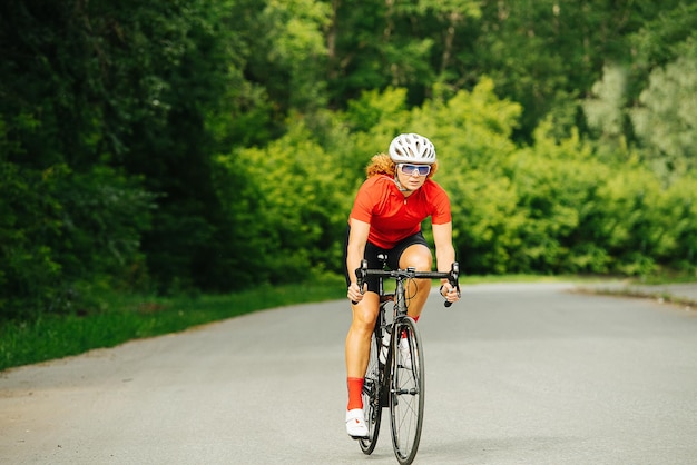 Wysportowana Kobieta Jedzie Na Rowerze Wyścigowym Drogą Przez Park Z Zarośniętymi Drzewami